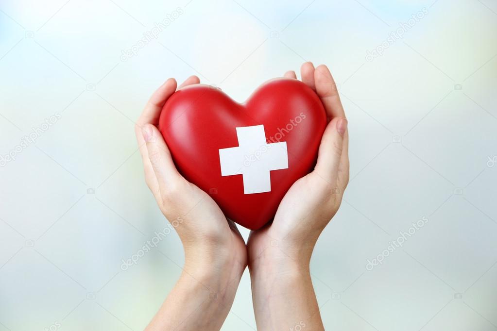 Red heart with cross sign in female hands