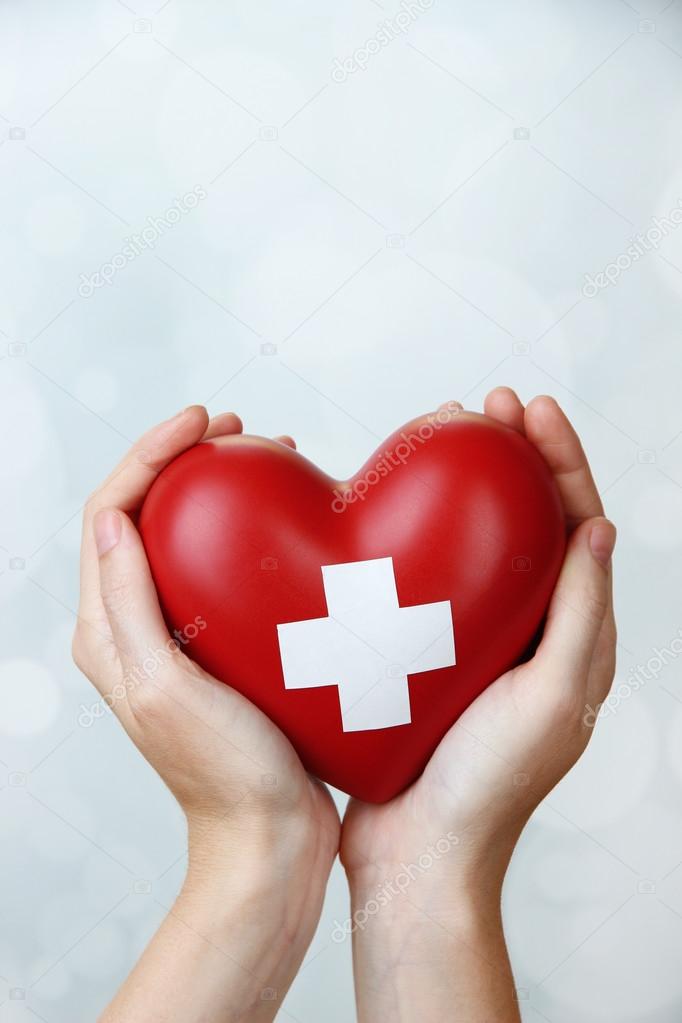 Red heart with cross sign in female hands