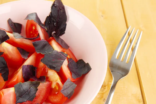 Salát z čerstvých rajčat s bazalkou listy v misce na dřevěné pozadí — Stock fotografie