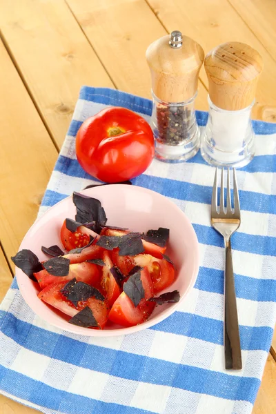 Salad of fresh tomatoes with basil leaves in a bowl on napkin on wooden background — Stock Photo, Image