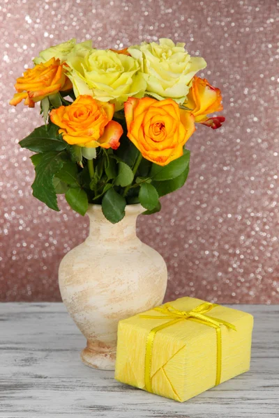 Bellissimo mazzo di rose in vaso con regalo su tavola su sfondo marrone — Foto Stock