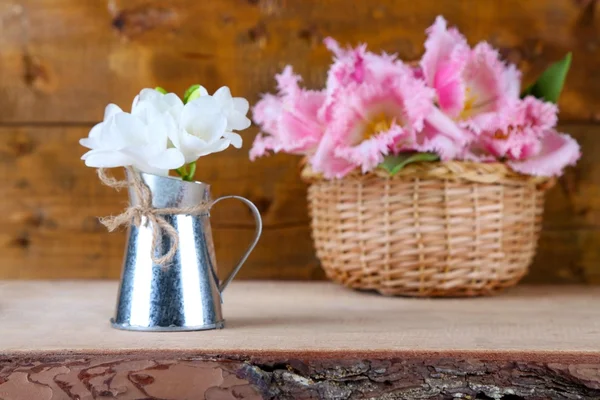 Mooie bloemen in vaas en rieten mand, op houten achtergrond — Stockfoto