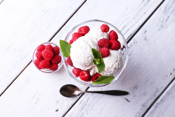 Gelato cremoso con lamponi su piatto in ciotola di vetro, su sfondo di legno a colori — Foto Stock