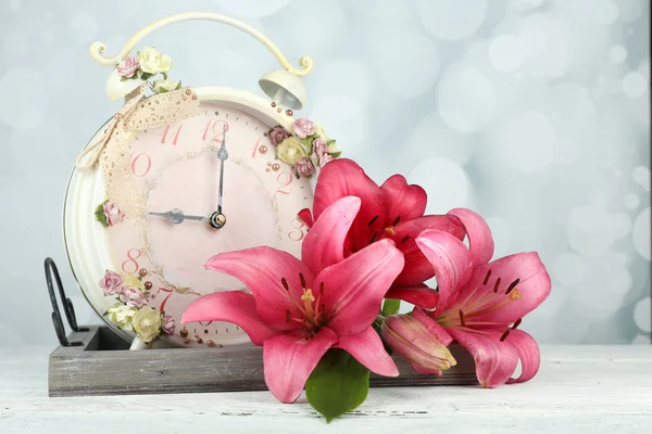 Beautiful lily with clock on wooden tray on bright background — Stock Photo, Image