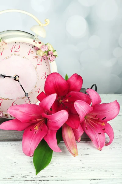 Beautiful lily with clock on wooden tray on bright background — Stock Photo, Image