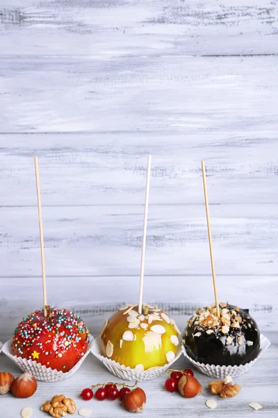 Sweet caramel apples on sticks with berries, on wooden table — Stock Photo, Image