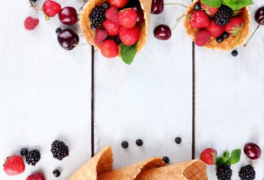 Beyaz ahşap zemin üzerinde şeker koni içinde farklı olgun çilek