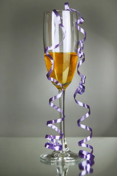 Bicchiere di champagne e streamer dopo la festa su sfondo grigio — Foto Stock