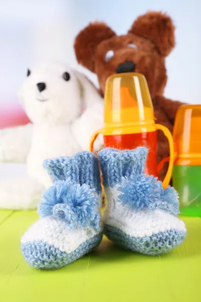 Composition with crocheted booties for baby, bottle, toy and other things on color background