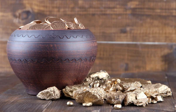 Moedas de ouro em vaso de cerâmica e pedaços de ouro, sobre fundo de madeira — Fotografia de Stock