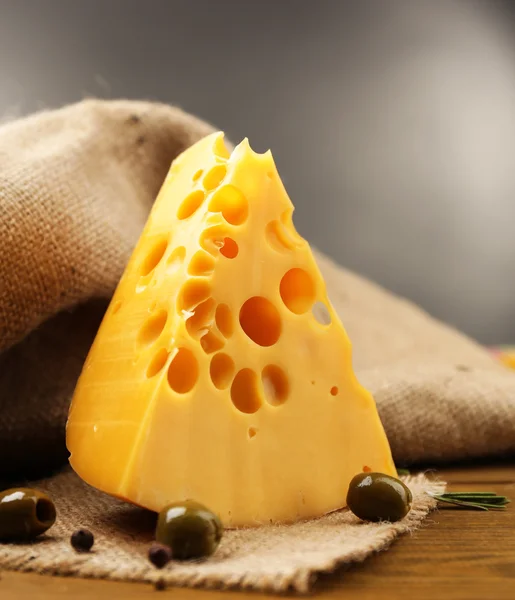 Morceau de fromage sur assiette aux olives vertes, sur table en bois, sur fond sombre — Photo