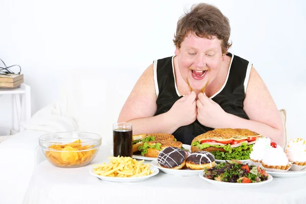 Толстяк имеет большой обед, на домашнем фоне интерьера — стоковое фото