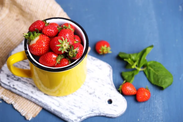 Maturare le fragole dolci in tazza su sfondo di legno di colore — Foto Stock