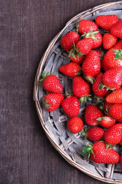 Maturare dolci fragole su stuoia di vimini, su sfondo di legno a colori — Foto Stock