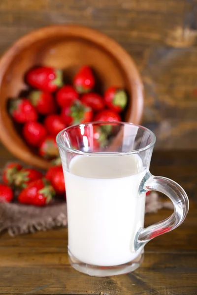 Ripe sweet strawberries in wooden bowl and glass with milk on color wooden background — Stock Photo, Image