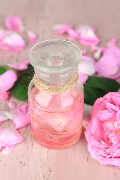 Olio di rosa in bottiglia su sfondo di legno di colore — Foto Stock