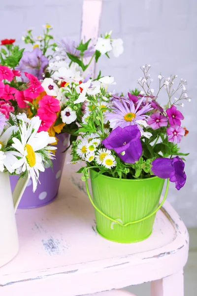 Bukett av färgglada blommor i dekorativa hinkar, på stol, på ljus vägg bakgrund — Stockfoto