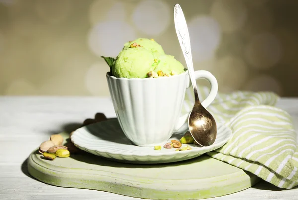 Crème glacée savoureuse à la pistache dans une tasse sur une table en bois, sur fond clair — Photo