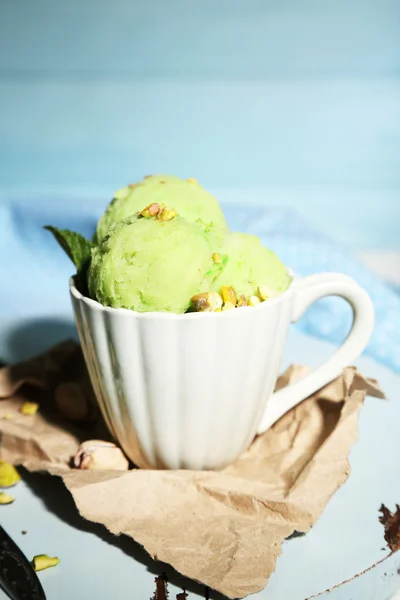 Tasty pistachio ice cream in cup on wooden table, on blue background — Stock Photo, Image