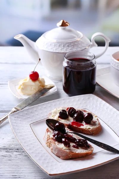 Pan fresco con mermelada de cereza y mantequilla casera en plato sobre mesa de madera, sobre fondo brillante — Foto de Stock