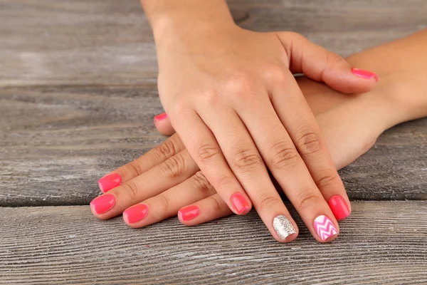 Mano femenina con elegantes uñas de colores, sobre fondo de madera — Foto de Stock