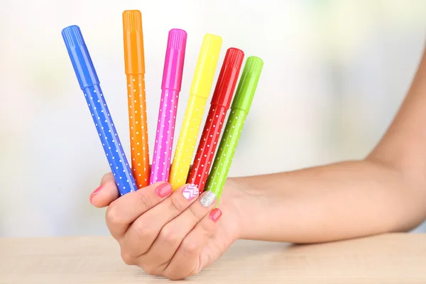 Mano femenina con elegantes uñas coloridas sosteniendo plumas de fieltro, sobre mesa de madera, sobre fondo brillante —  Fotos de Stock