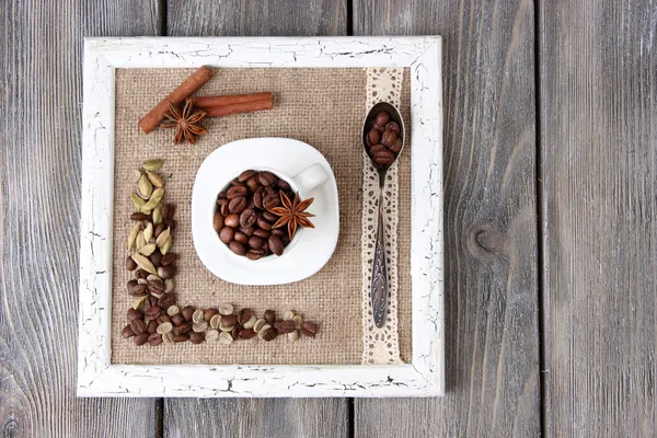 Bingkai kayu dengan cangkir putih, biji-bijian kopi dan rempah-rempah di latar belakang kayu — Stok Foto