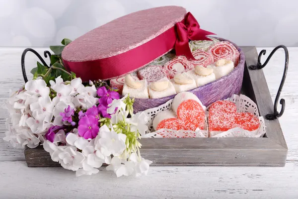 Caja de regalo con dulces y flores en la mesa sobre fondo brillante — Foto de Stock