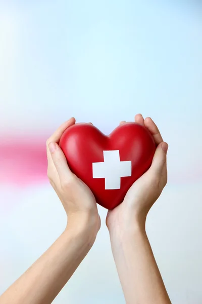 Red heart with cross sign in female hand, close-up, on light background — Stock Photo, Image