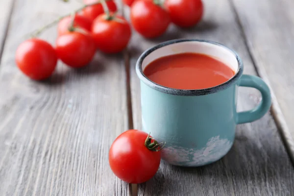 Sumo de tomate caseiro na caneca a cores e tomates frescos no fundo de madeira — Fotografia de Stock