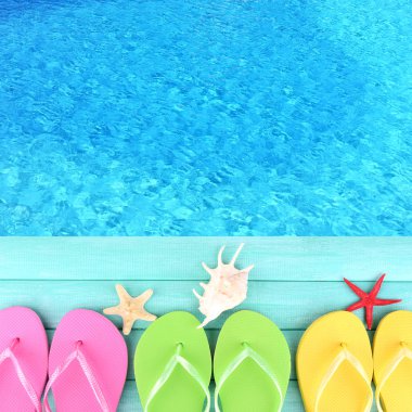 Colored flip flops on wooden platform beside sea clipart