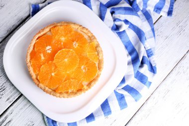 Homemade orange tart on plate, on color wooden background