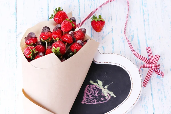 Aardbei in chocolade op spiesjes in papieren zak op tabel close-up — Stockfoto