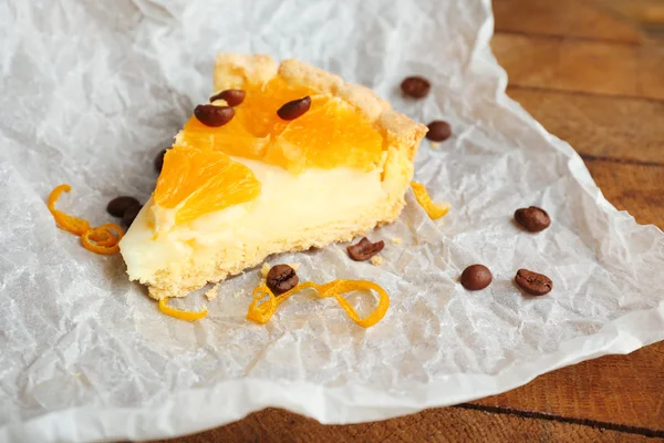 Pedaço de torta de laranja caseira no guardanapo de papel, na cor de fundo de madeira — Fotografia de Stock