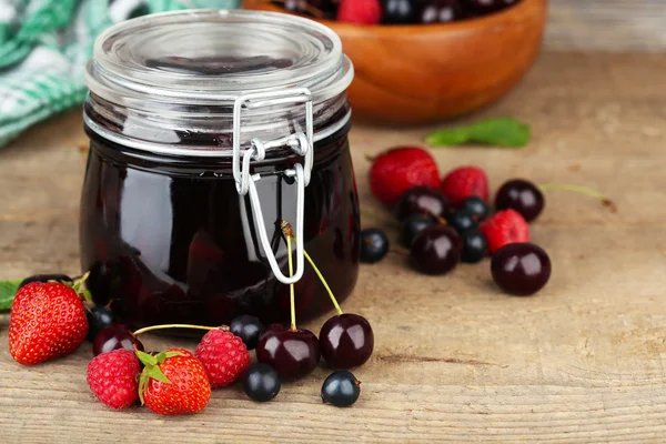 Smakelijke jam met bessen in glazen pot op houten tafel — Stockfoto