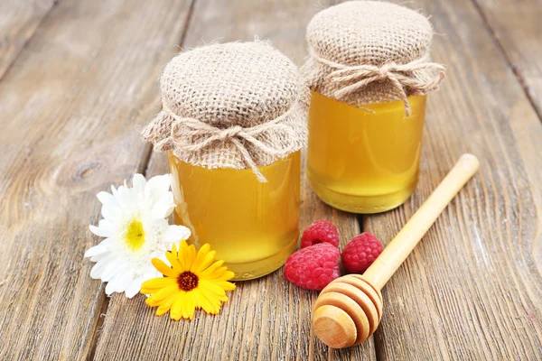 瓶がいっぱいのおいしい新鮮な蜂蜜、木製テーブルの上の野生の花 — ストック写真