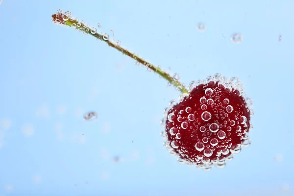 Hermosa cereza en agua con burbujas, sobre fondo azul — Foto de Stock