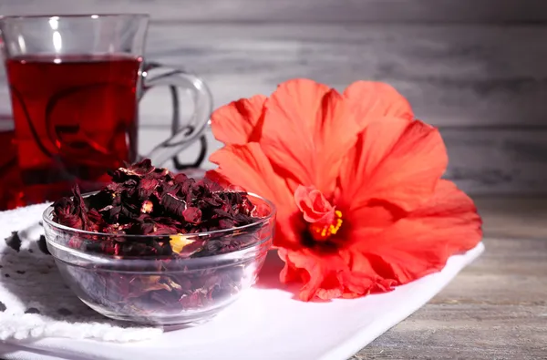 Hibiskus te i glas tekanna och blomma på färg servett på trä bakgrund — Stockfoto