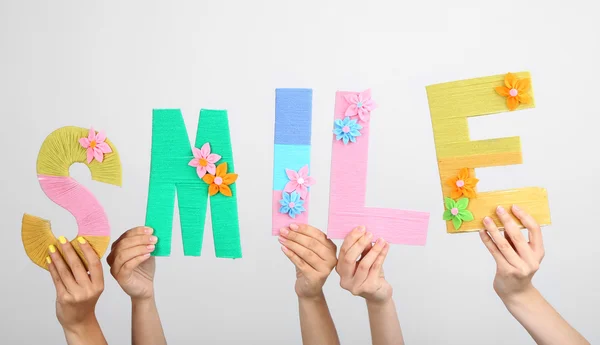 Manos levantando letras construyendo una sonrisa de palabra sobre fondo gris —  Fotos de Stock