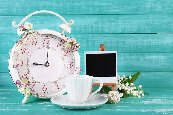 Beautiful vintage alarm clock with flowers and cup of tea on blue wooden background — Stock Photo, Image