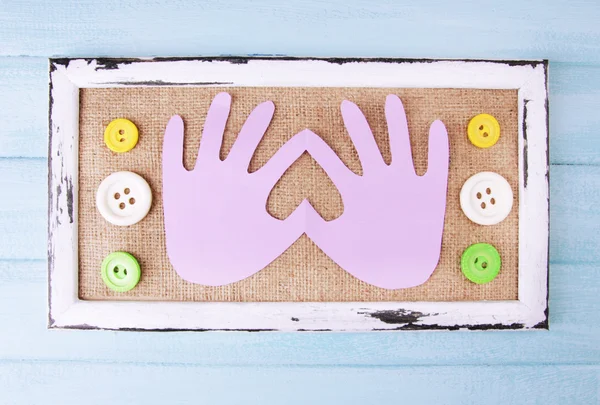 Wooden frame with paper arms and colorful buttons on wooden background — Stock Photo, Image