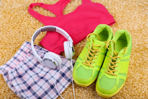 Sportbekleidung, Schuhe und Kopfhörer auf farbigem Teppich-Hintergrund. — Stockfoto