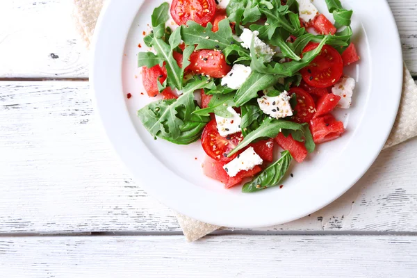 Salad with watermelon, feta, arugula and basil leaves on plate, on wooden background — Stock Photo, Image