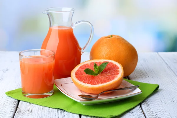 Half of grapefruit, glass jug with fresh juice and spoon on plate on light background — Stock Photo, Image