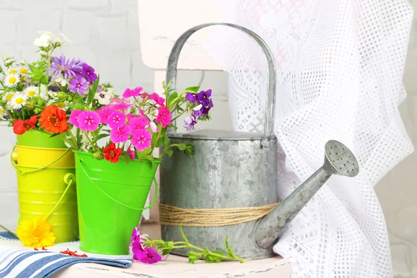 Bouquet of colorful flowers in decorative buckets, on chair, on light wall background — Stock Photo, Image