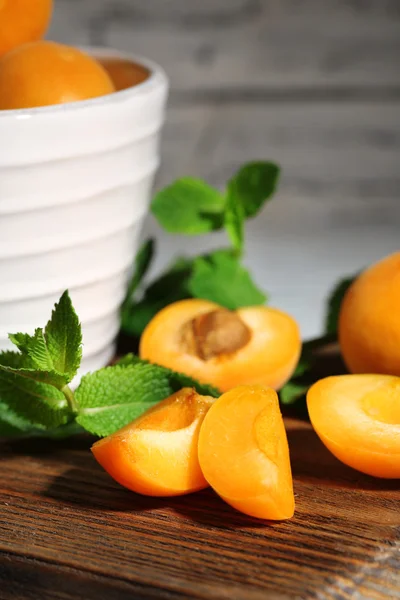 Ripe apricots with green mint leaves on cutting board, on wooden background — Stock Photo, Image