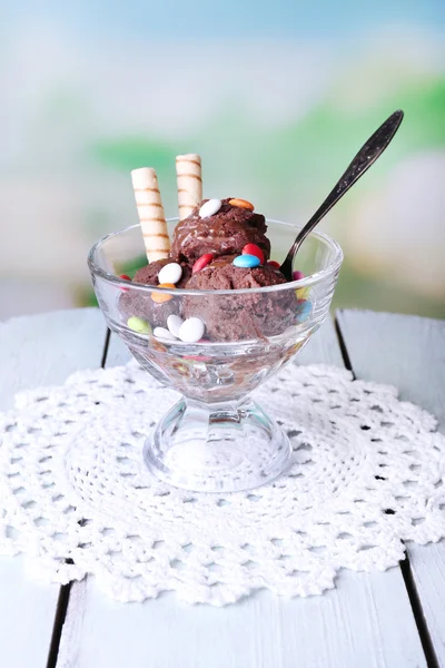 Helado de chocolate con caramelos multicolores y rollos de oblea en cuenco de vidrio, sobre mesa de madera de color, sobre fondo brillante —  Fotos de Stock