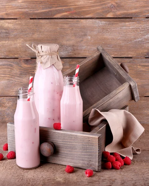 Botellas de sabrosas bebidas batidas de frambuesa sobre fondo de madera rosa gris — Foto de Stock