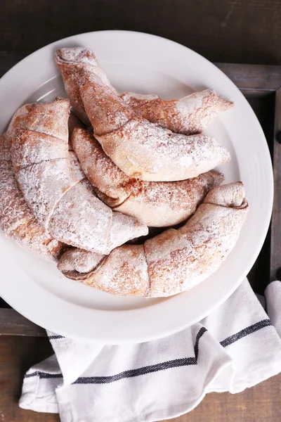 Tasty bagels with powdered sugar on tray, on wooden background — Stock Photo, Image