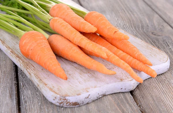 Fresh carrot on cutting board on wooden background — Stock Photo, Image